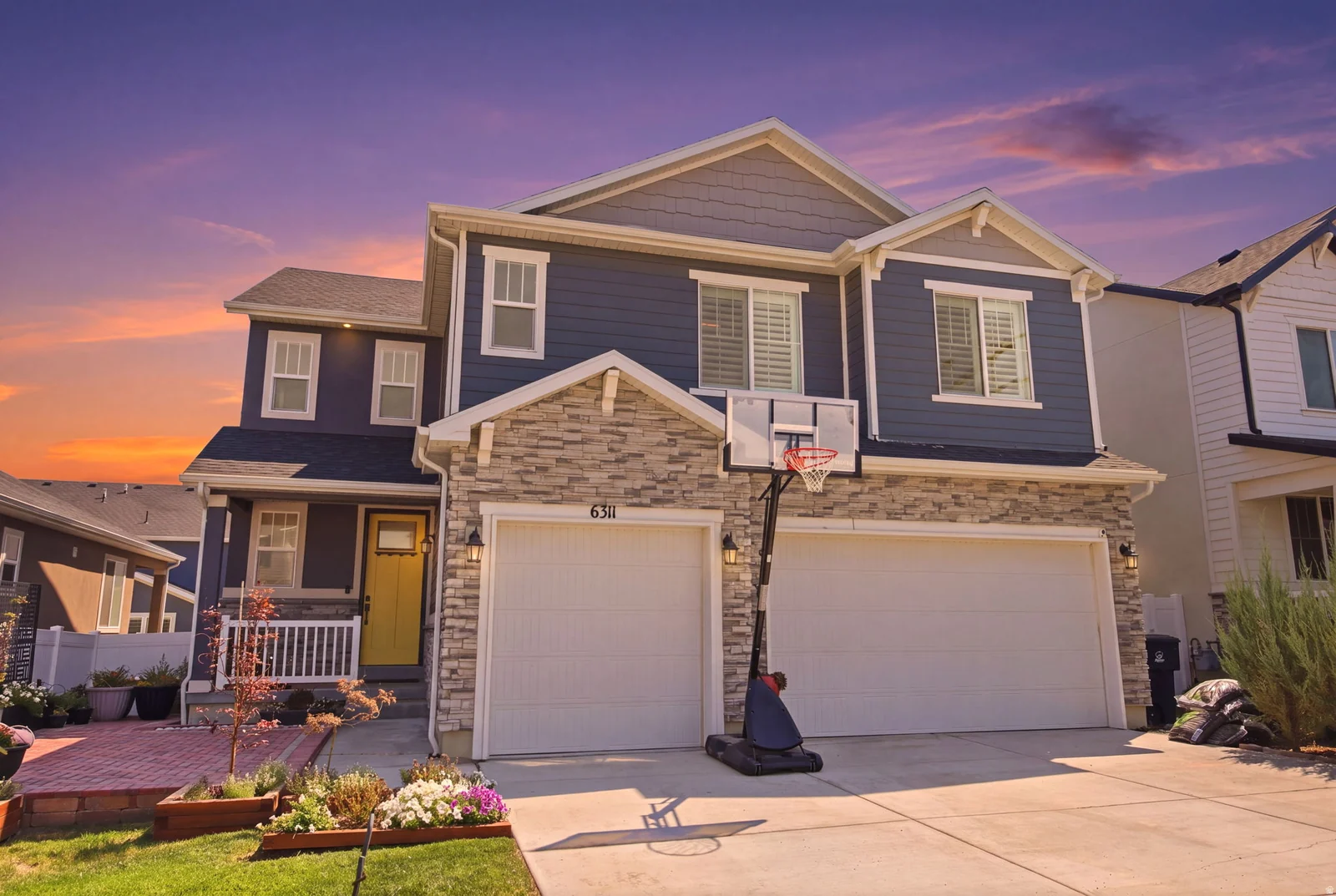 Two-story residence featuring a stone and siding facade, a two-car garage, and a welcoming yellow front door